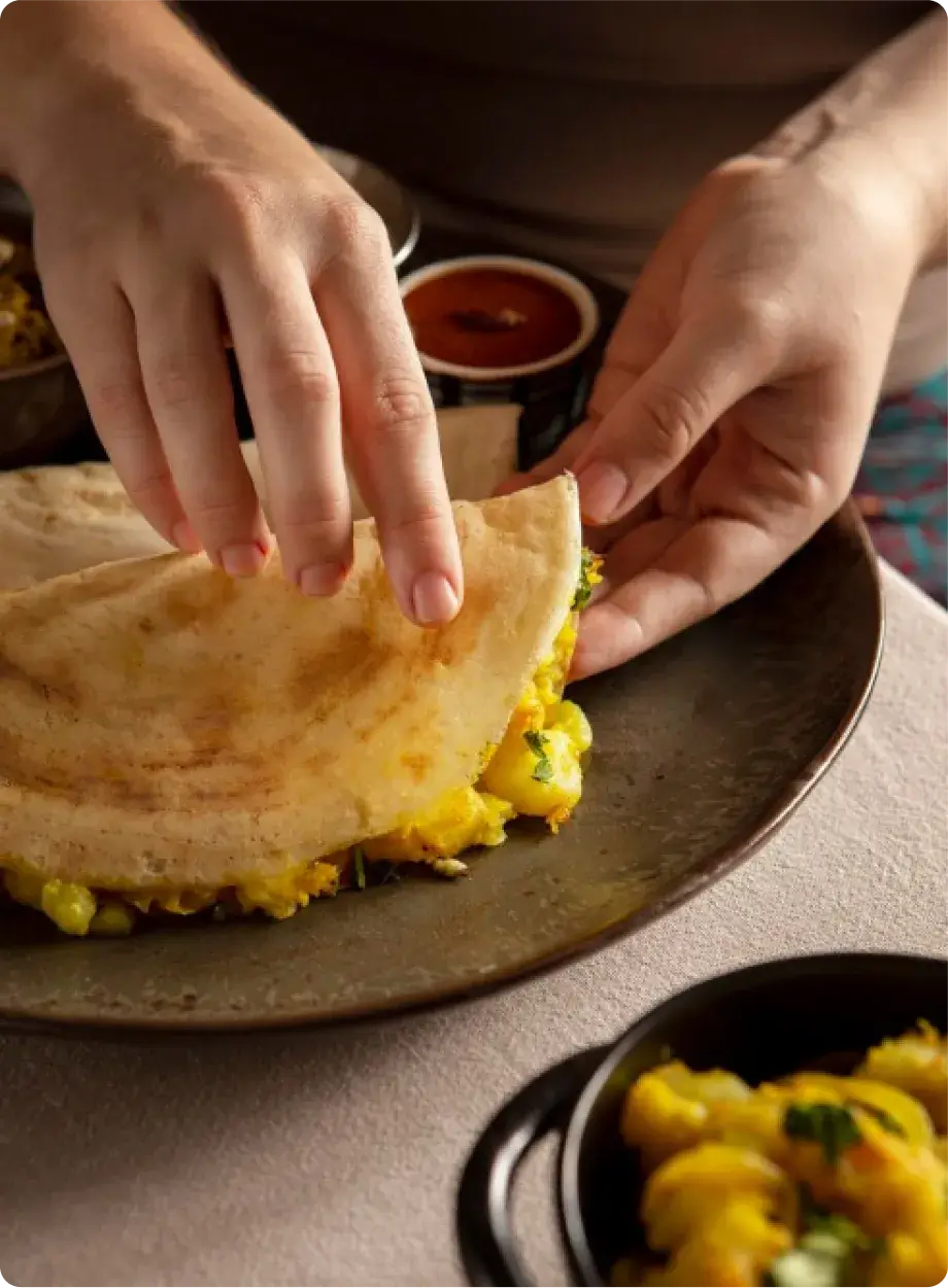 Close-up of hands folding a dosa filled with spiced potato mix